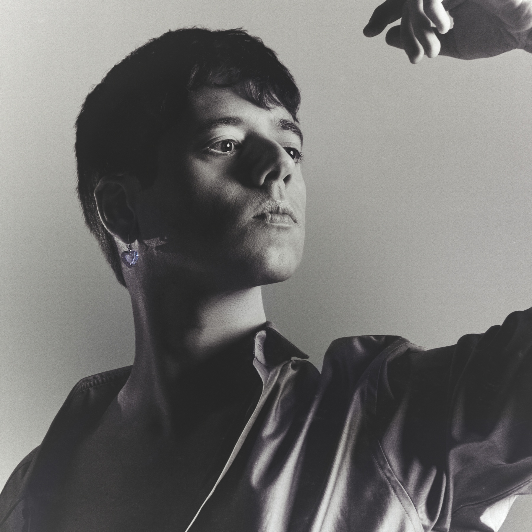 A person poses with raised hand in dramatic black and white portrait photography.