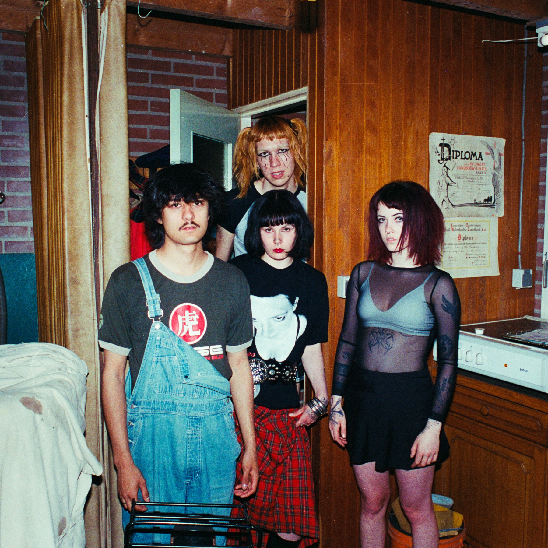 Four young people pose in a vintage interior with wood paneling and retro decorations.