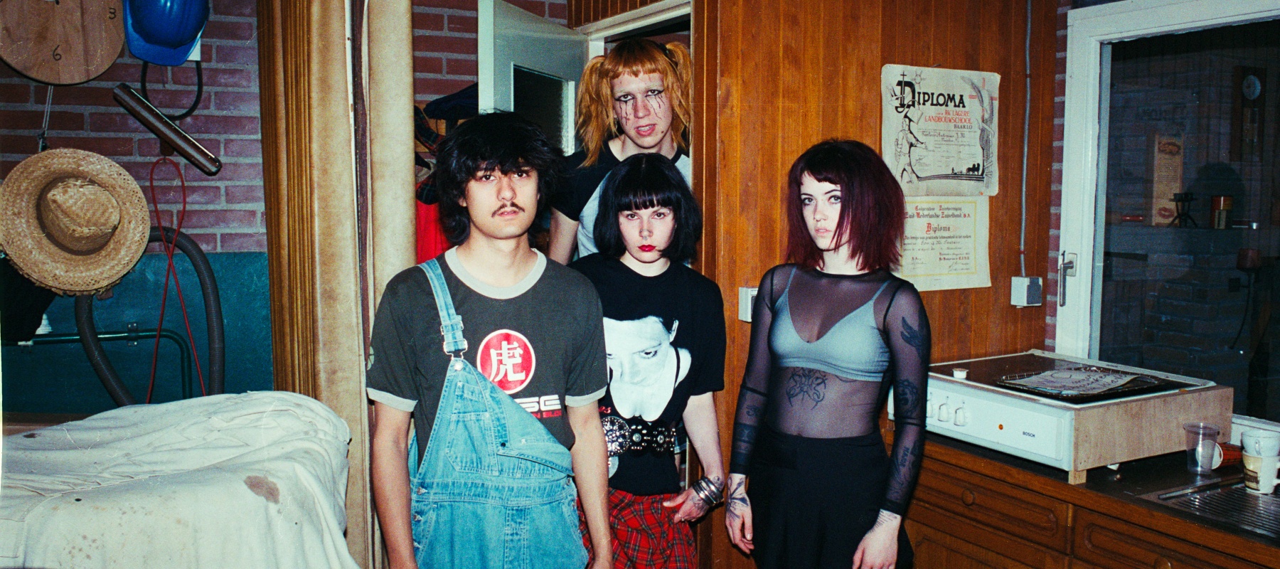 Four young people pose in a vintage interior with wood paneling and retro decorations.