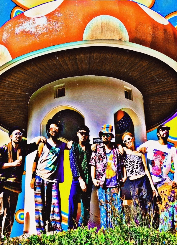 Six people standing in fornt of a big mushroom-shaped house