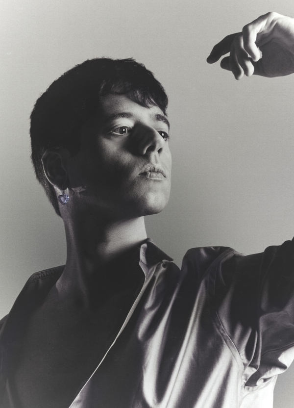 A person poses with raised hand in dramatic black and white portrait photography.